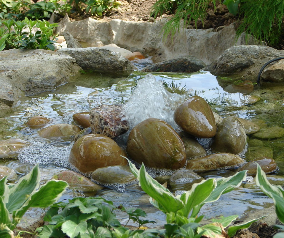 Sprudelnde Quelle umgeben von Steinen in einem kleinen Teich.