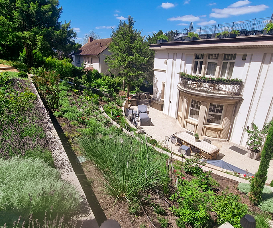 Am Hang liegender Garten und sonnige Terrasse sowie Haus.