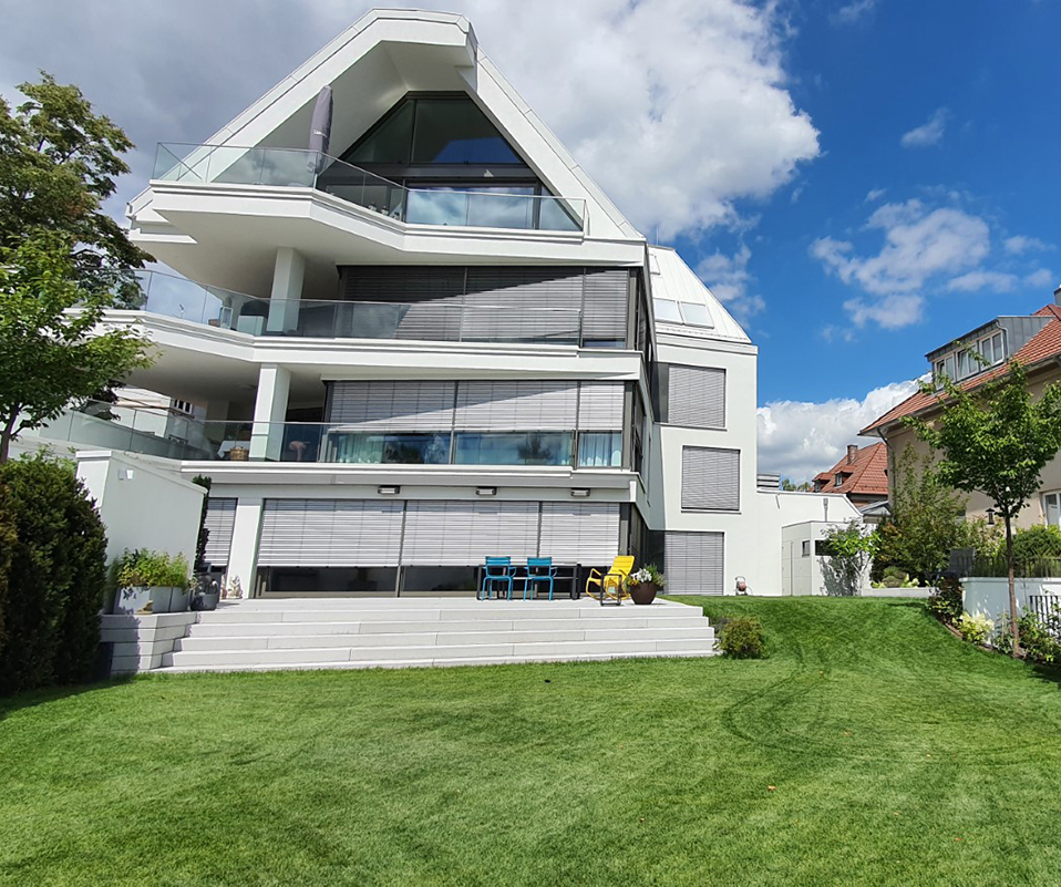 Großes Haus mit gepflegtem Rasen und einer breiten Treppe, die zu einer Terrasse führt.