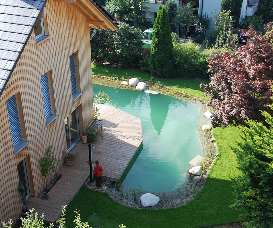 Großes Holzhaus mit einem ums Haus verlaufendem Schwimmteich.