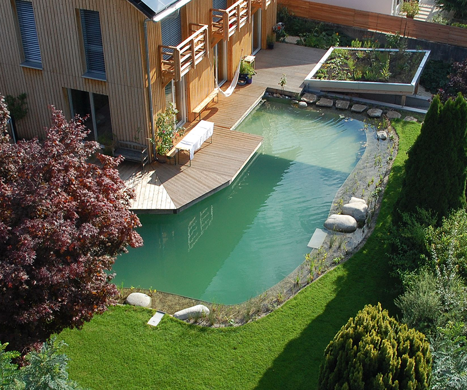 Großes Holzhaus mit einem ums Haus verlaufendem Schwimmteich.